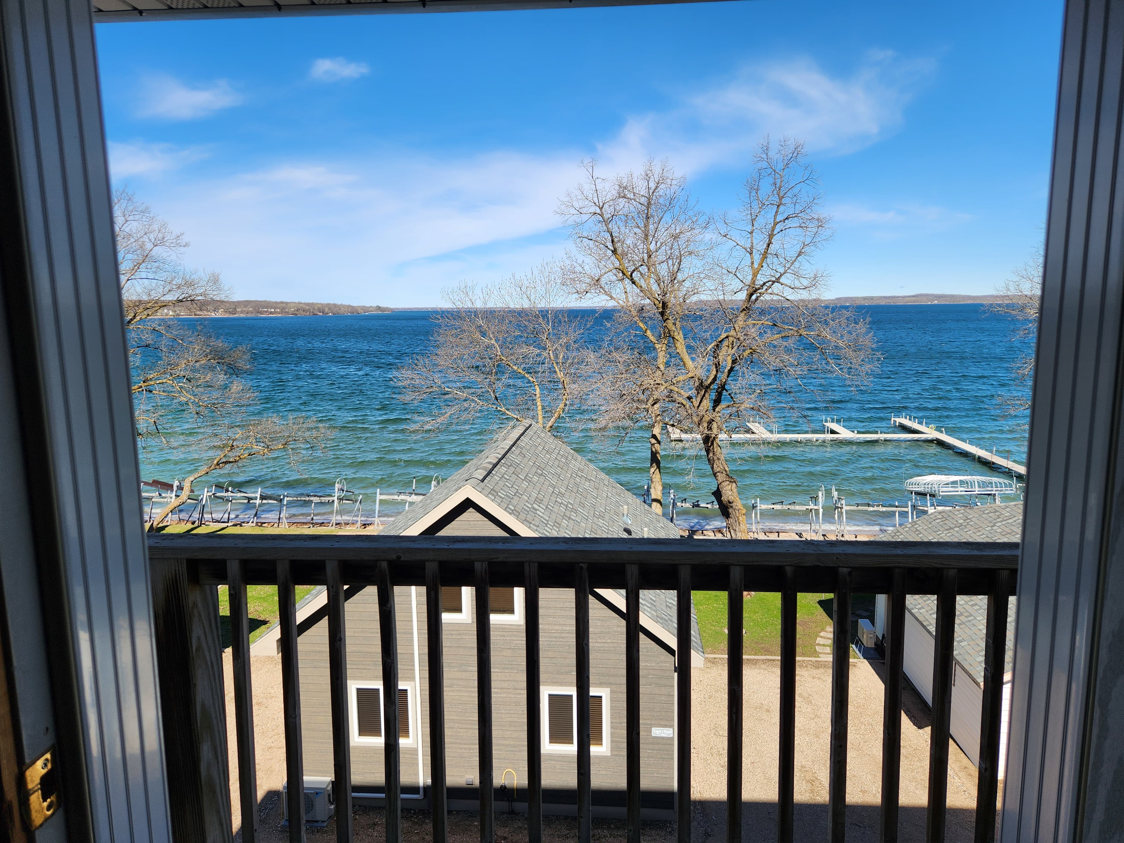 View from a balcony overlooking a lake and shoreline with trees and a boat dock.