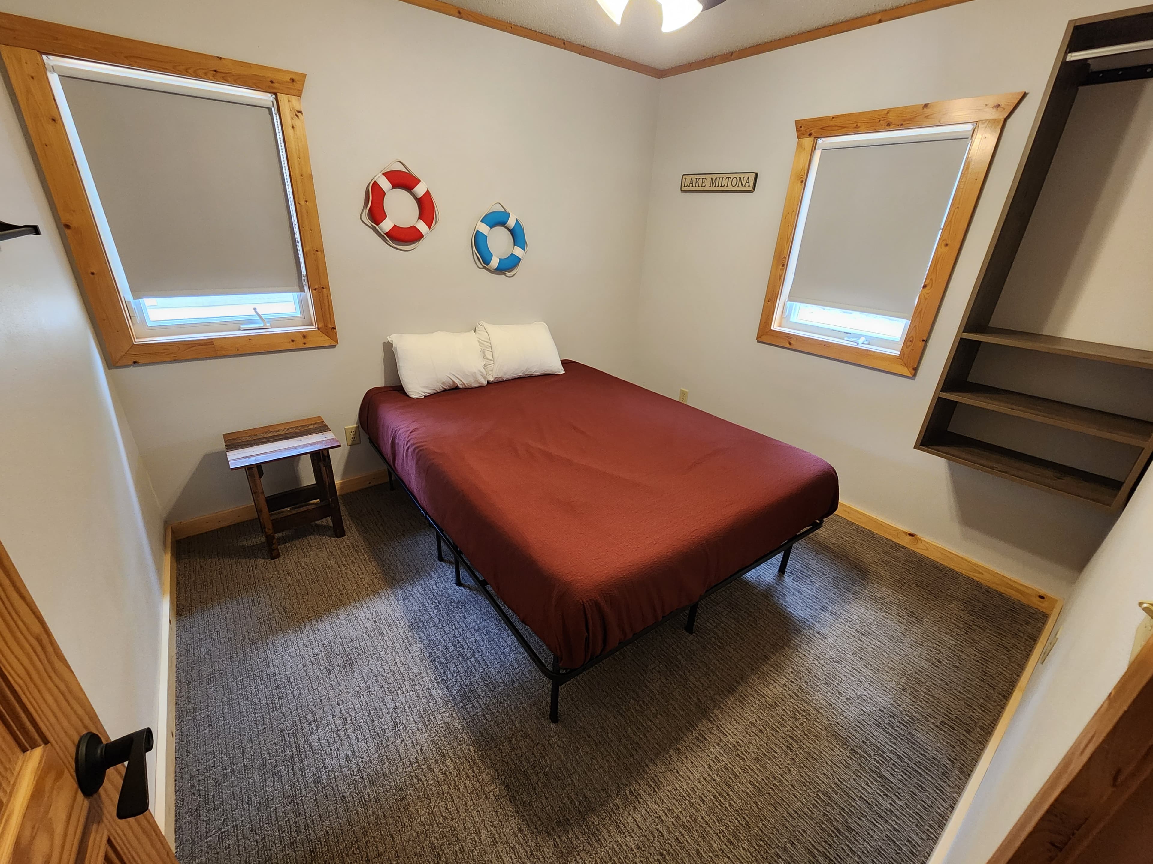 A cozy bedroom with a brown bed, a small wooden table, colorful wall decor, and shelves.