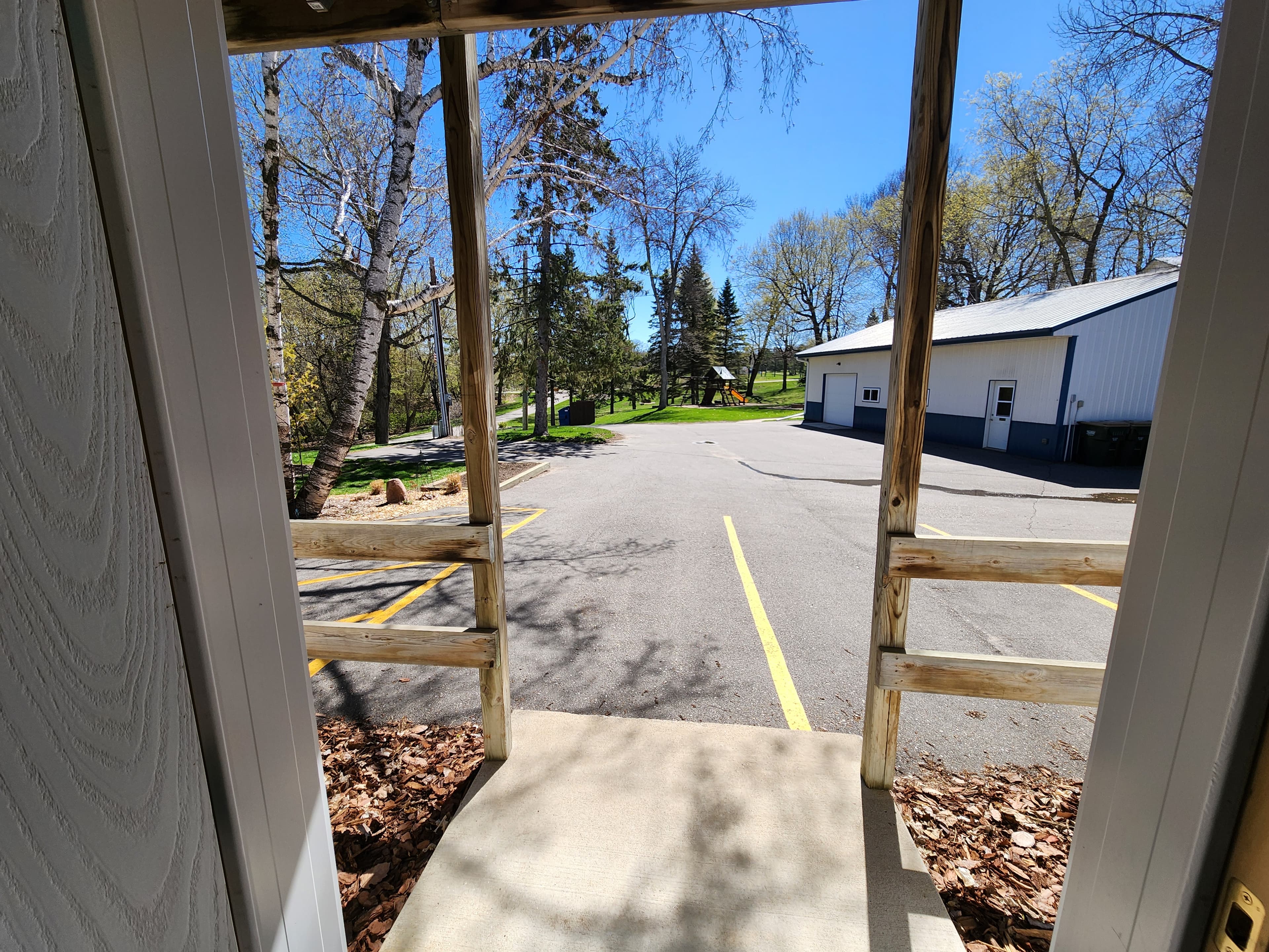 View from a doorway looking out onto a paved area and green space with trees in the background.