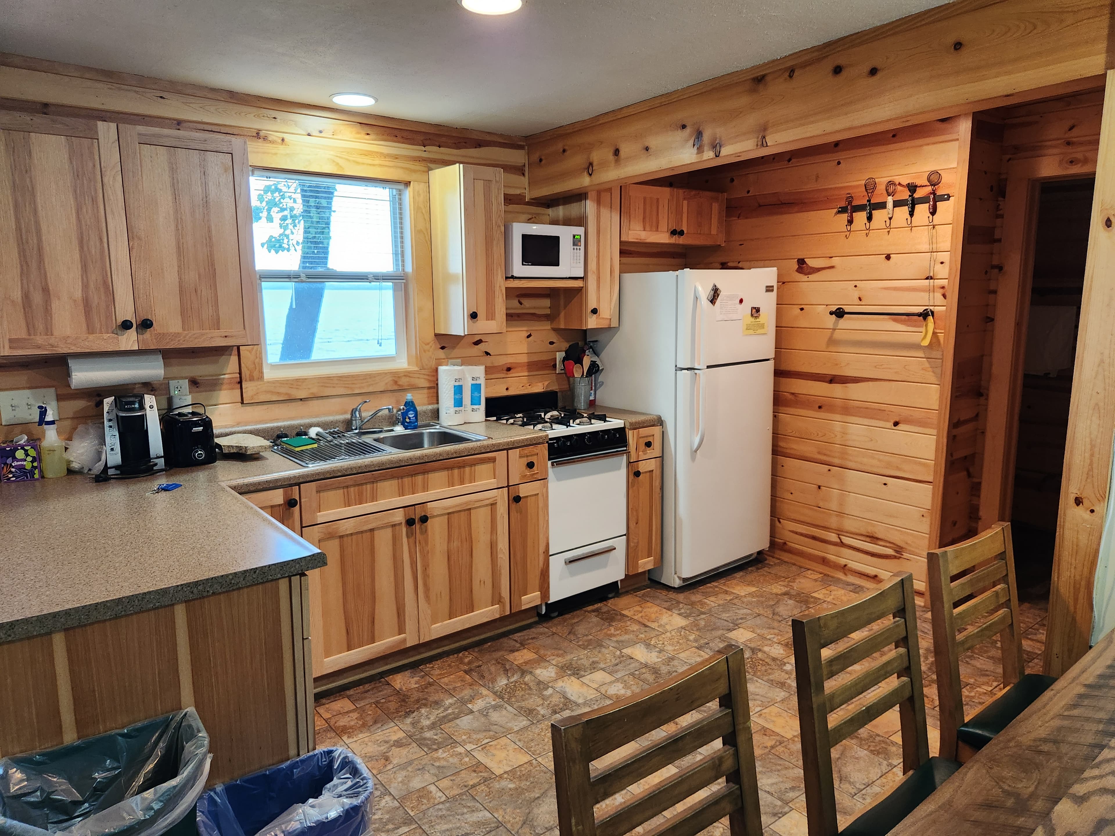 A cozy wooden kitchen featuring a stove, refrigerator, and counter space with chairs.