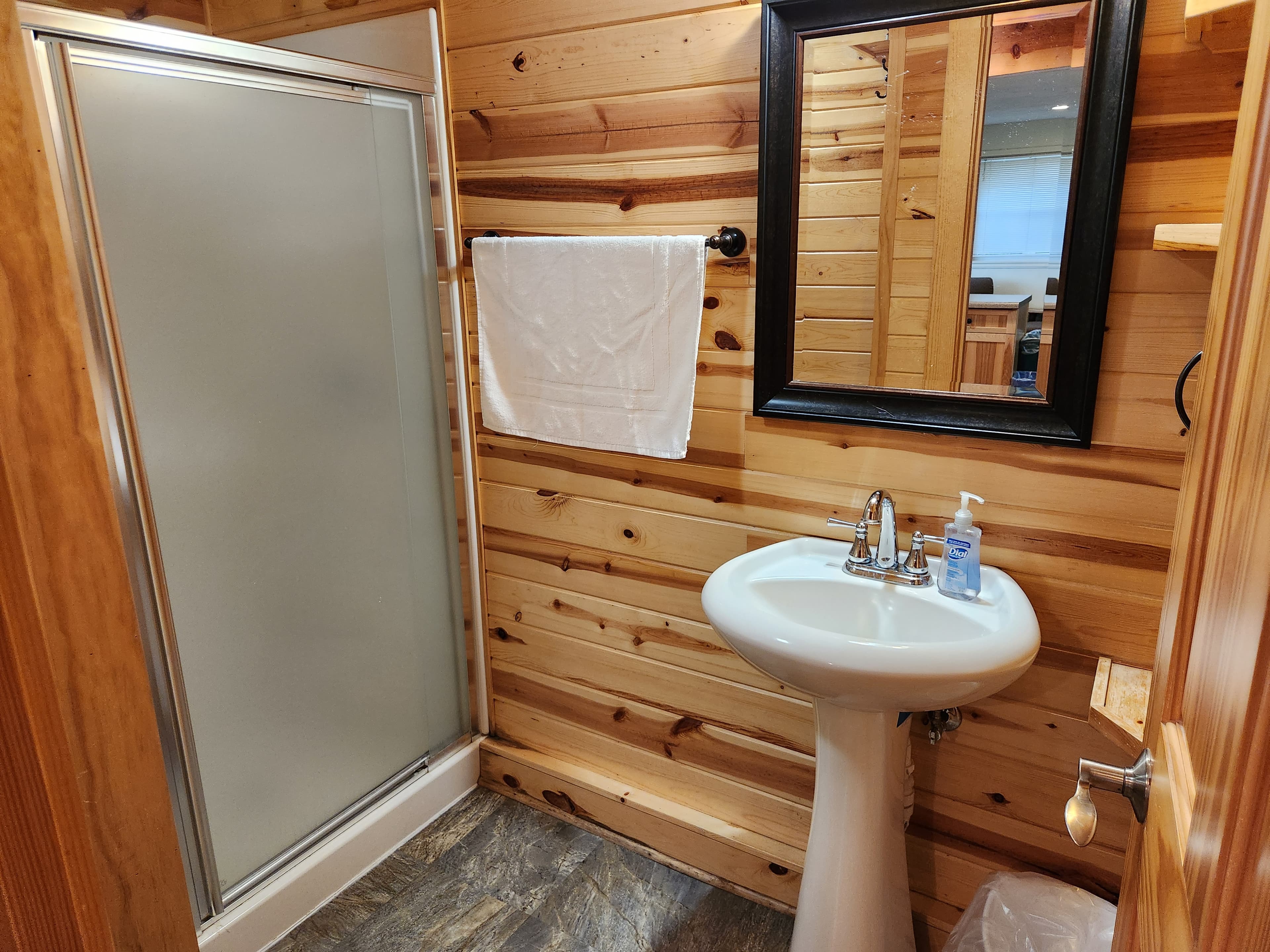 A compact bathroom featuring a shower, sink, and wooden walls.