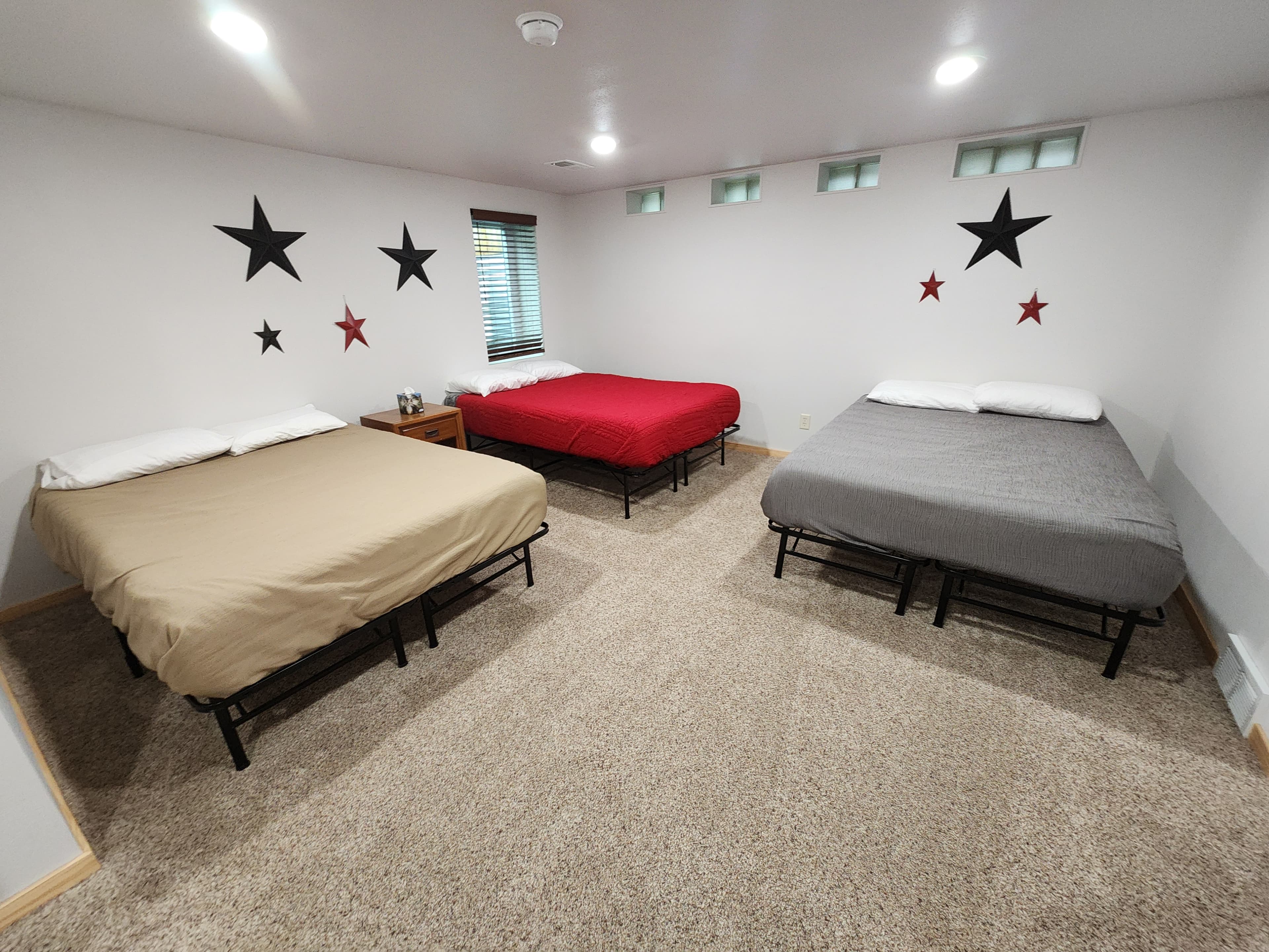 A spacious bedroom with three beds in beige, red, and gray, decorated with black and red stars on the walls.