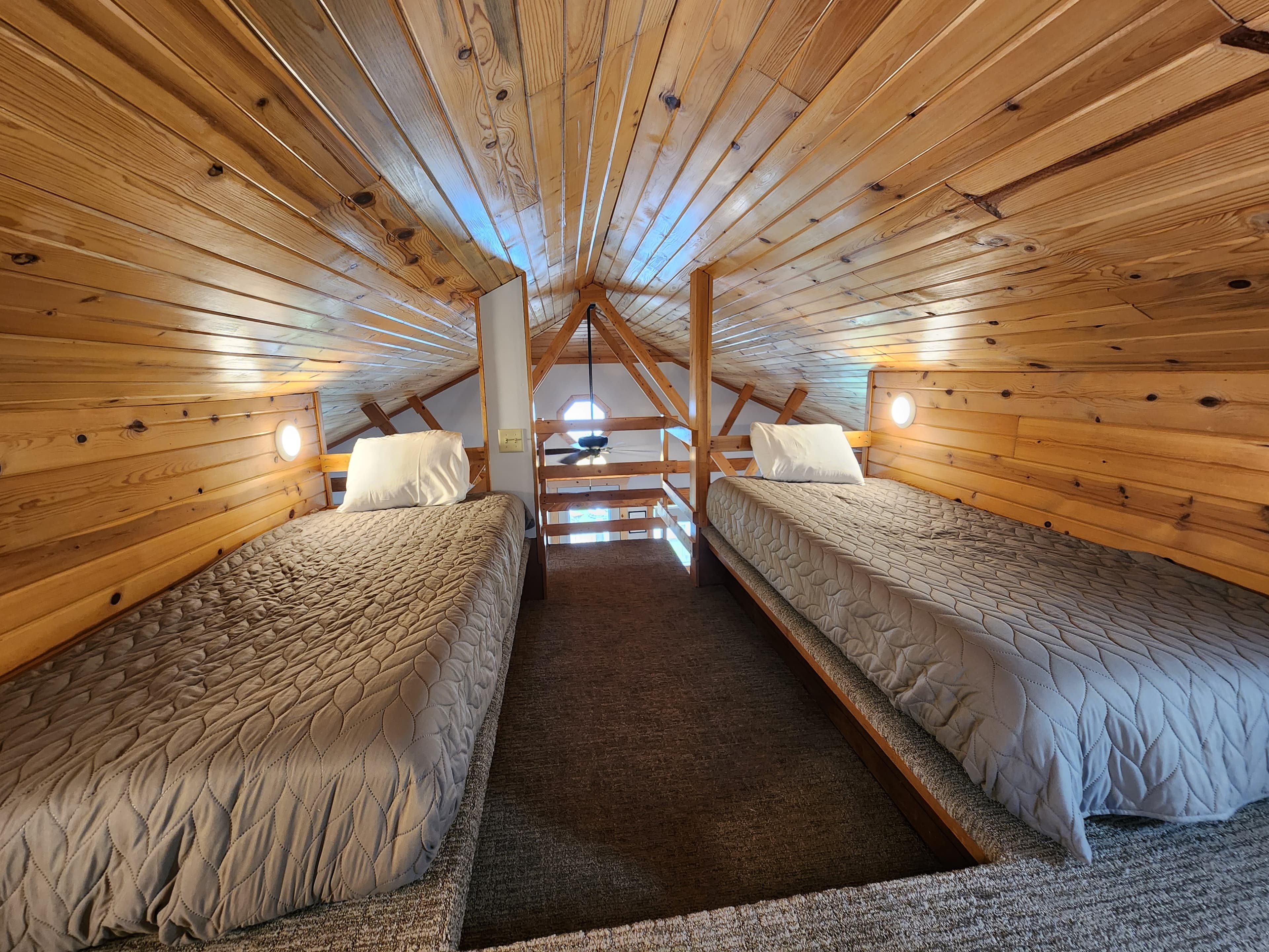 A cozy loft featuring two twin beds with wooden paneling and soft lighting.
