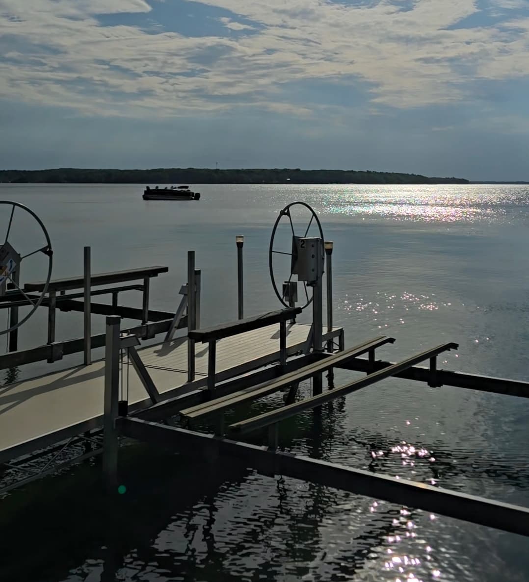 A serene lake scene with a dock, boat, and shimmering water under a cloudy sky.
