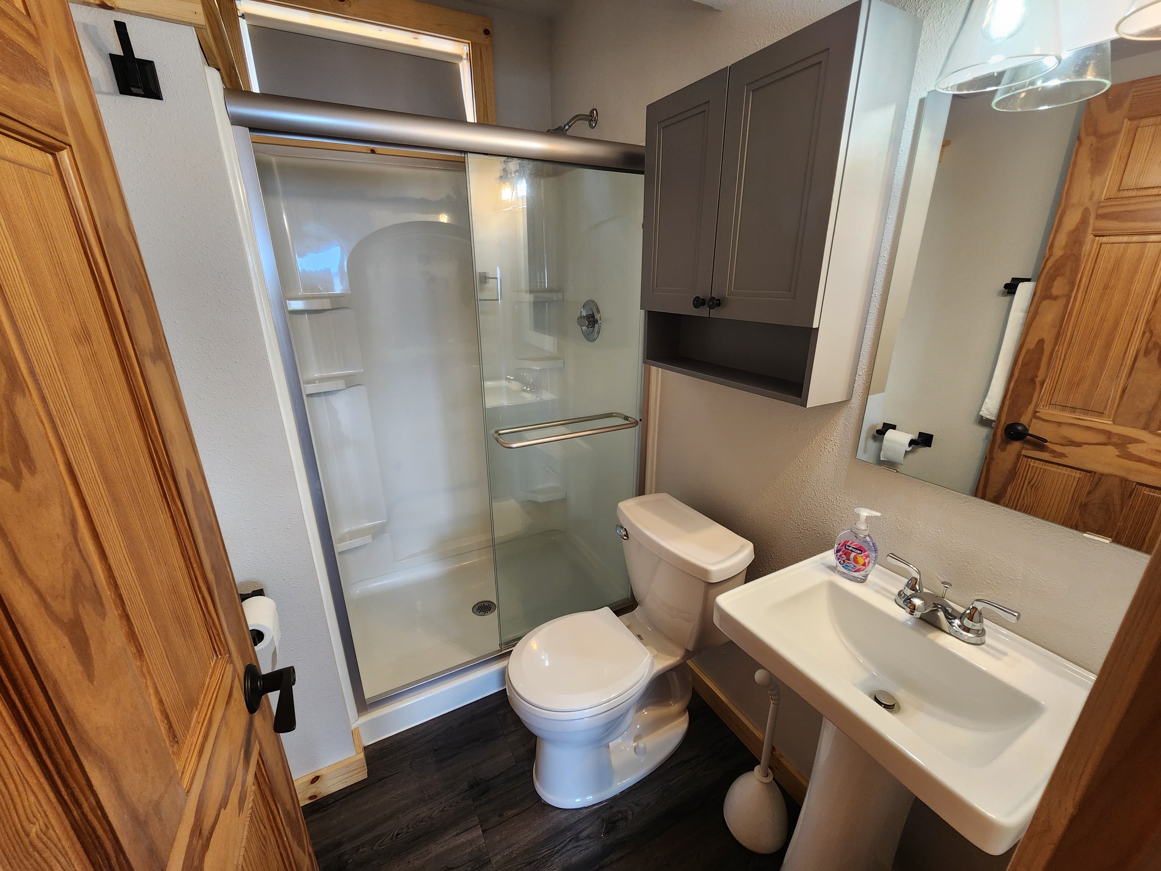 A small bathroom featuring a shower, toilet, and sink with wooden accents.
