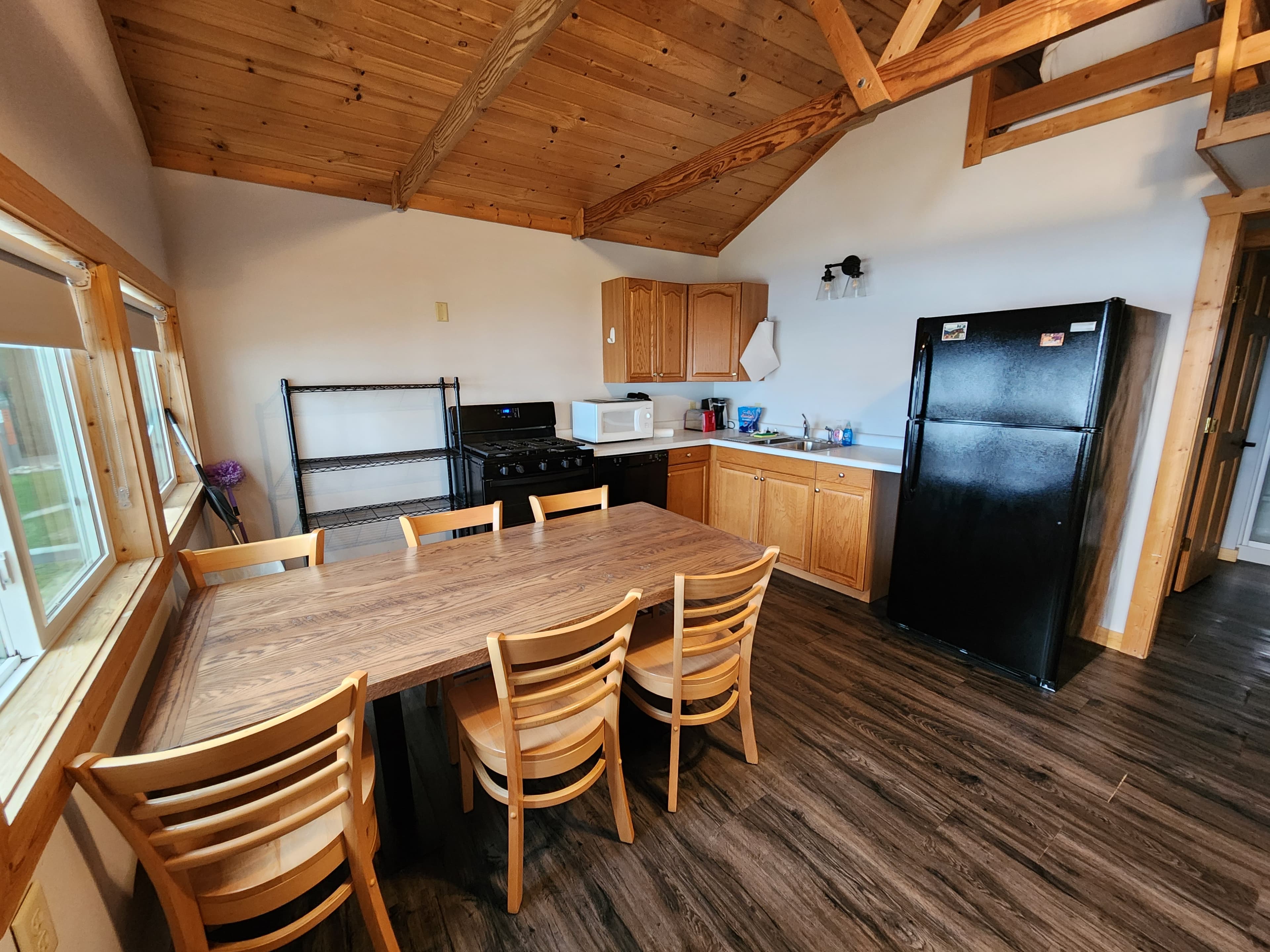 A modern kitchen with wooden cabinets, black appliances, and a large dining table surrounded by chairs.