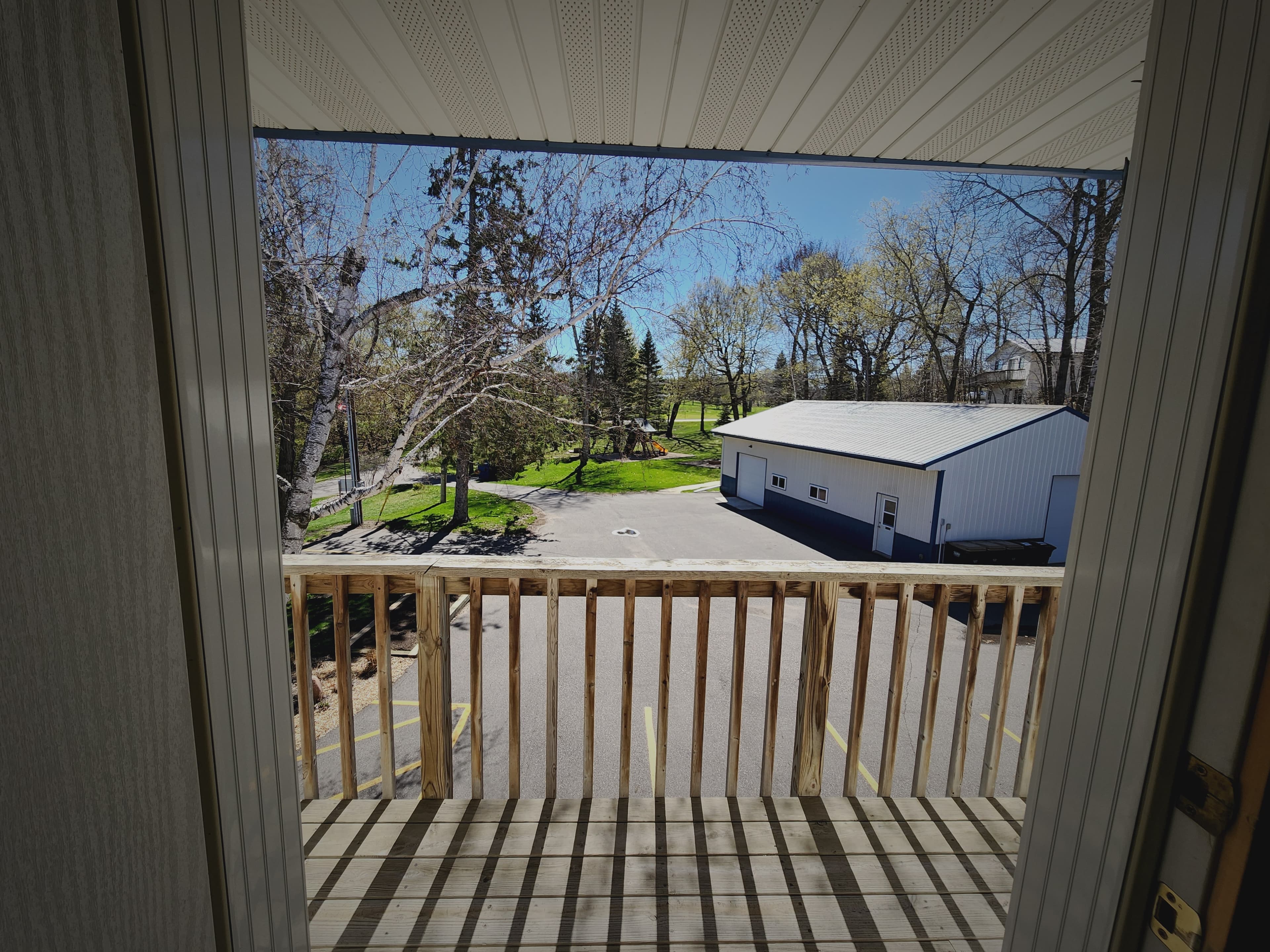 View from a balcony overlooking a parking lot and green trees on a sunny day.