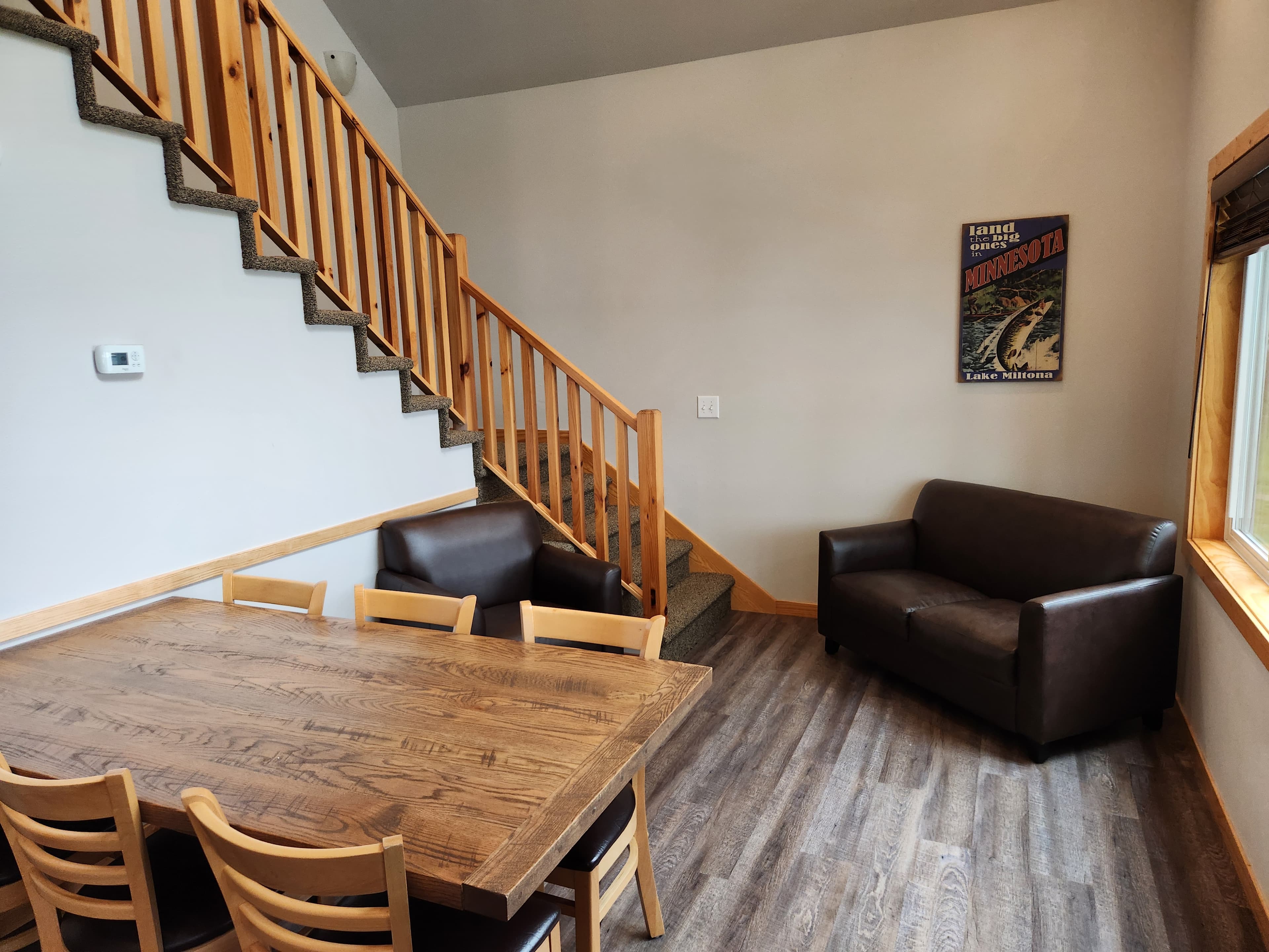 A cozy dining area with a wooden table and chairs, a dark brown sofa, and a staircase leading to the upper floor.