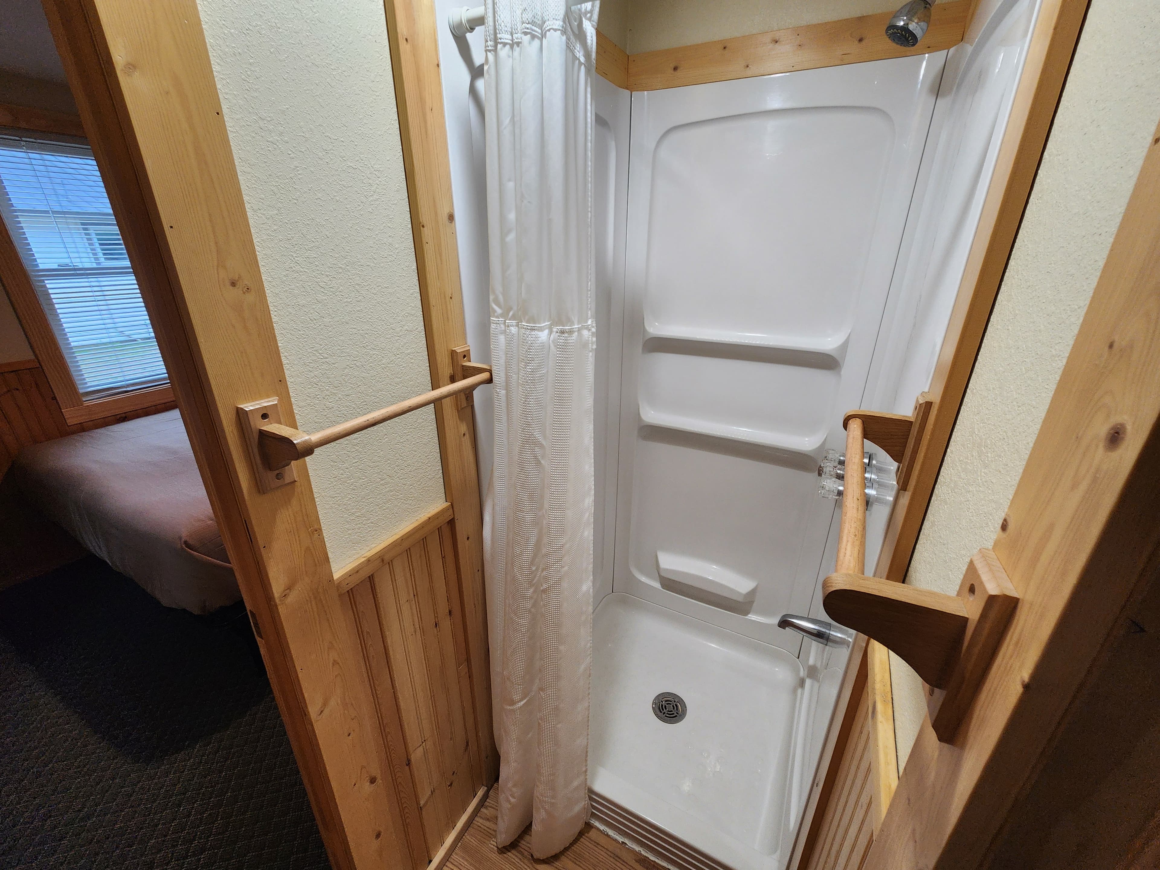 A small bathroom shower enclosed with a curtain and wooden accents.