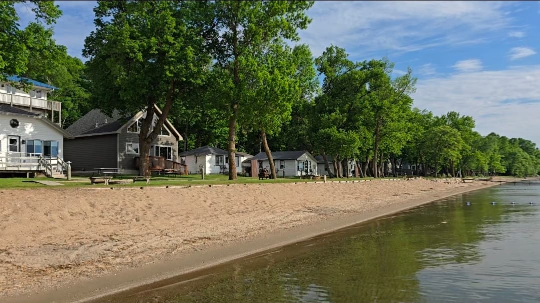 A sandy beach lined with cottages and trees under a clear blue sky.