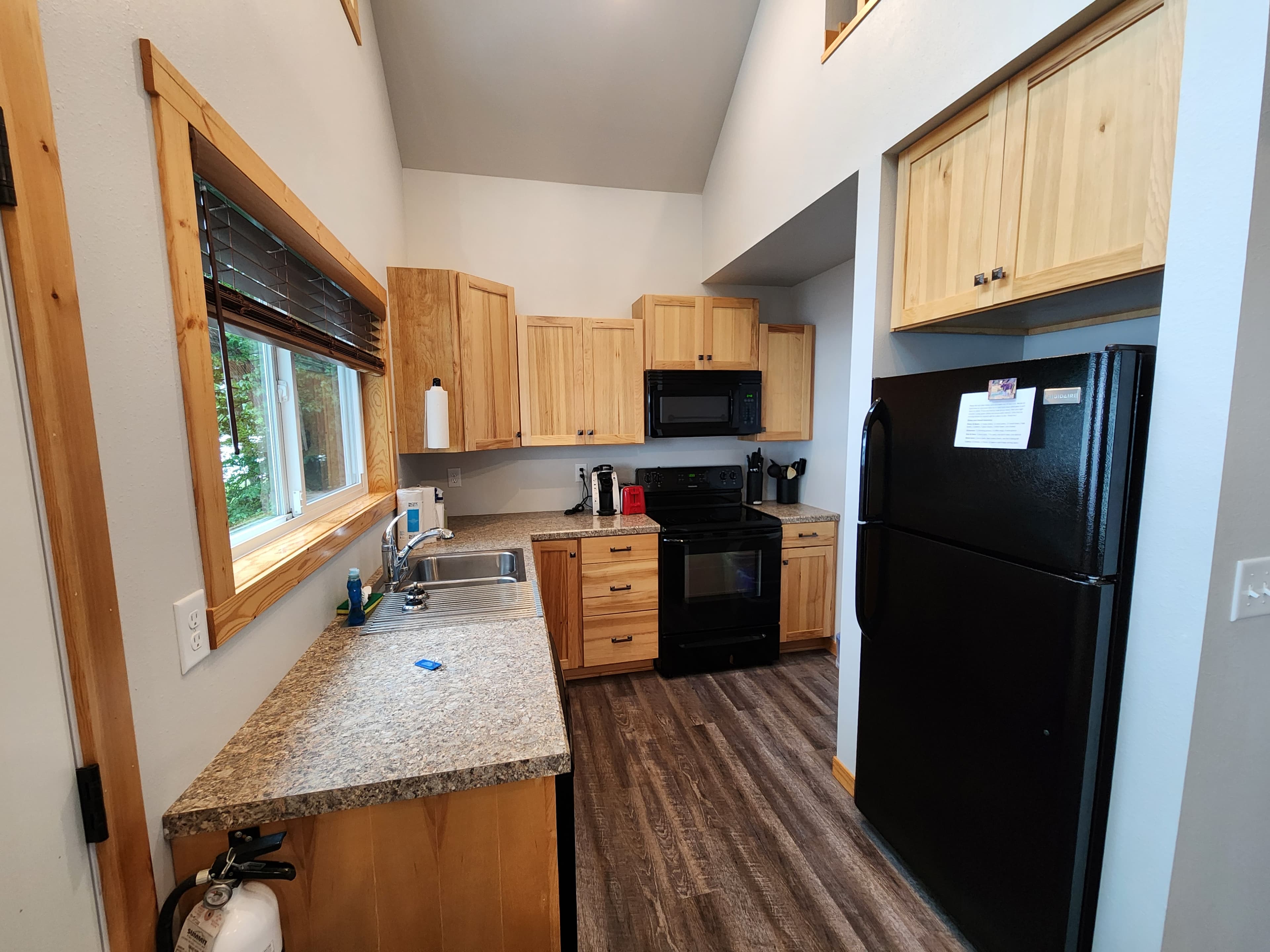 A modern kitchen with wooden cabinets, black appliances, and natural light from a window.