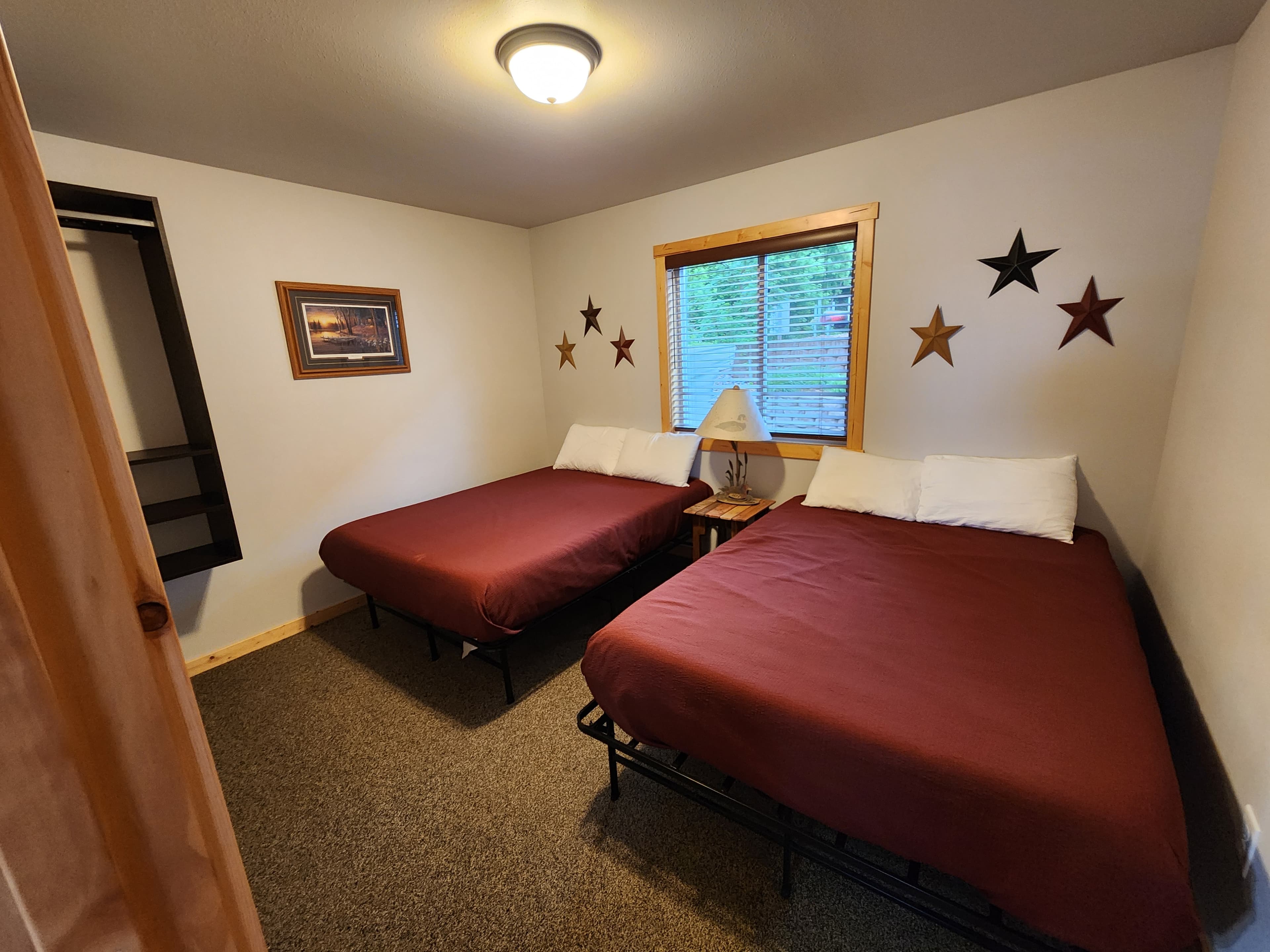 A cozy room featuring two twin beds with maroon covers, a window, and star decorations on the wall.
