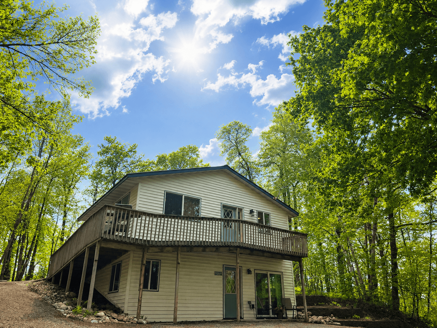 A modern house nestled among lush green trees under a bright blue sky.