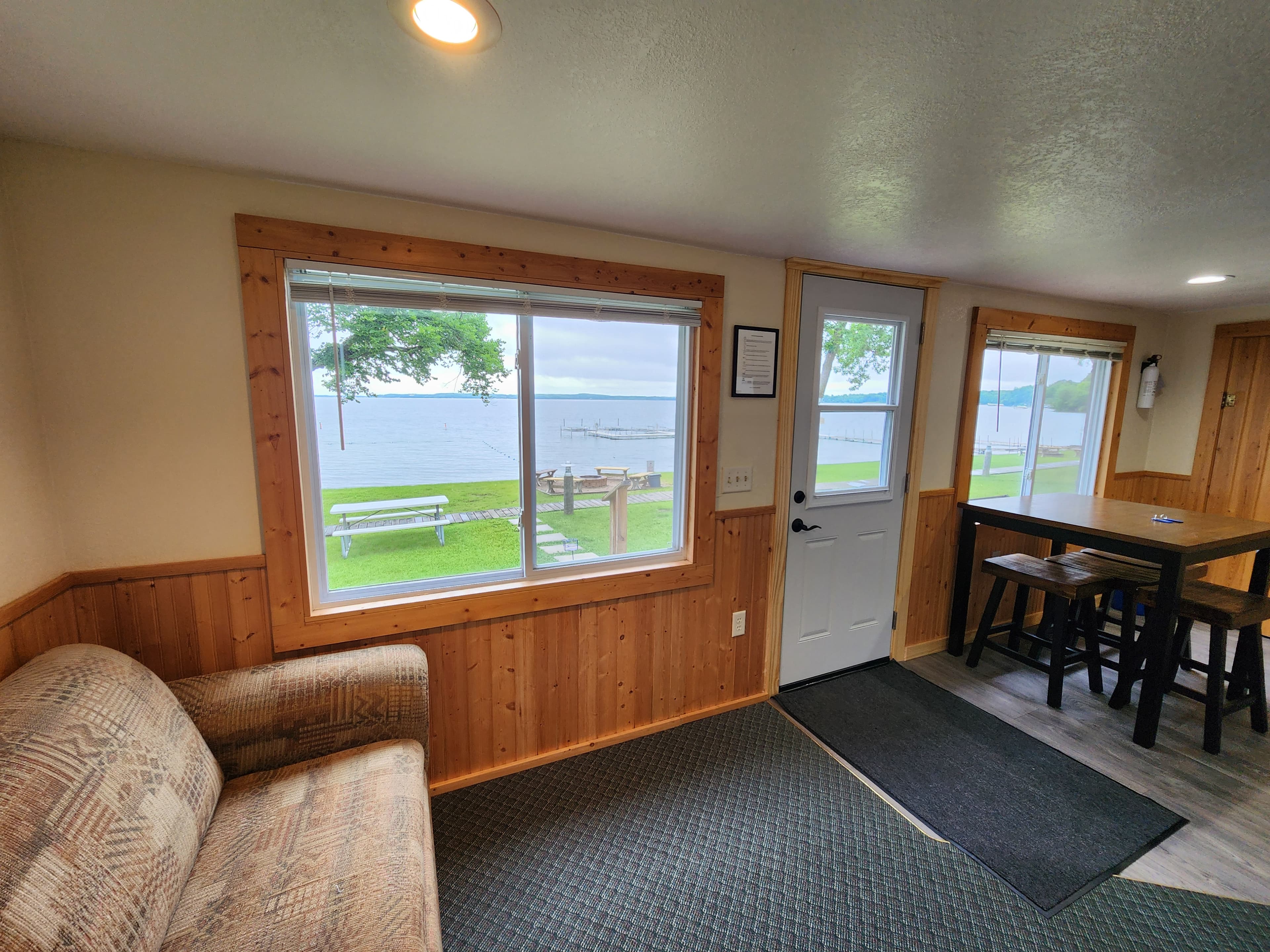A cozy interior room with a window view of a lake and outdoor seating.