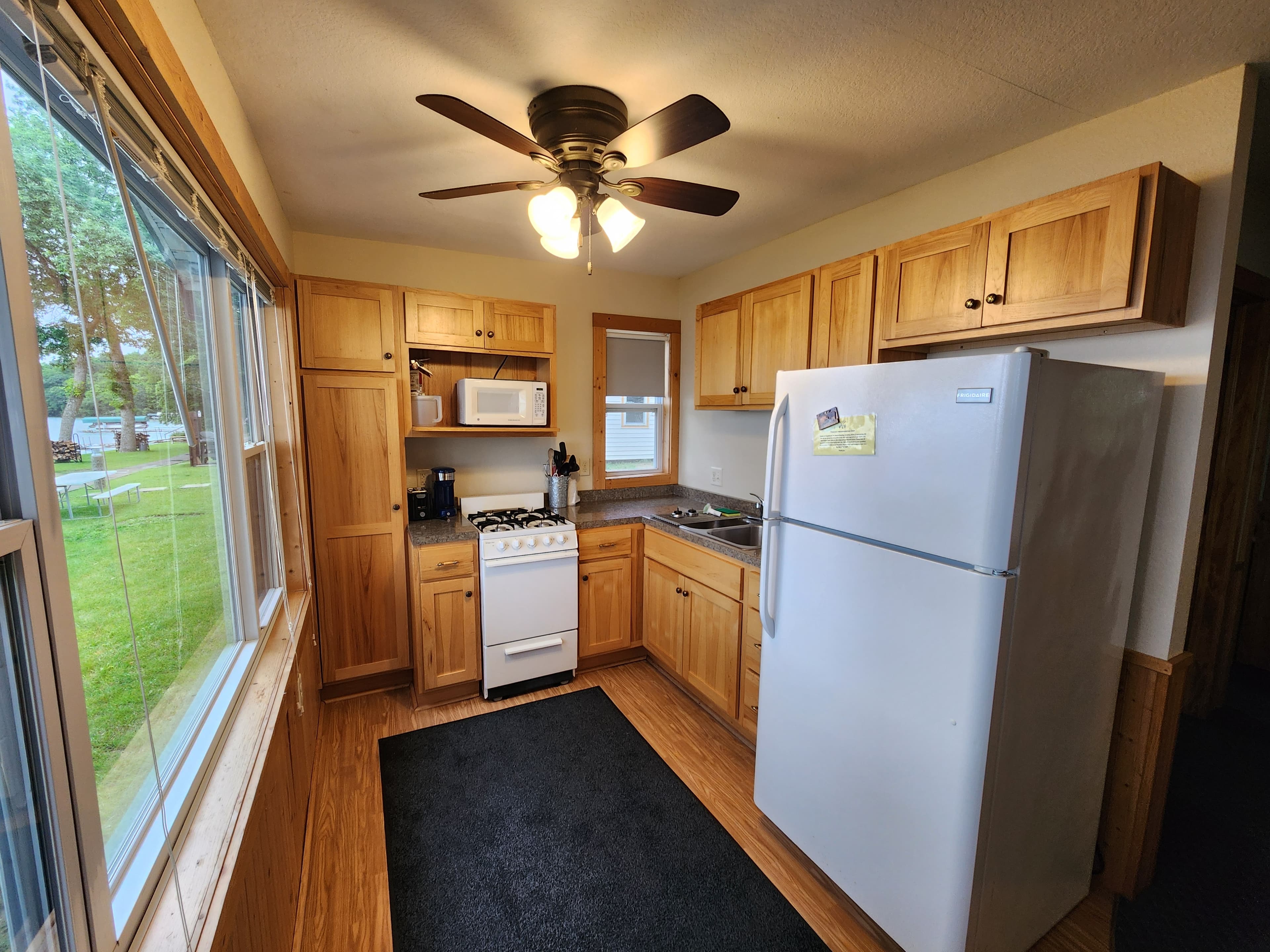 A cozy kitchen featuring wooden cabinets, a white refrigerator, a stove, and a window with a view.