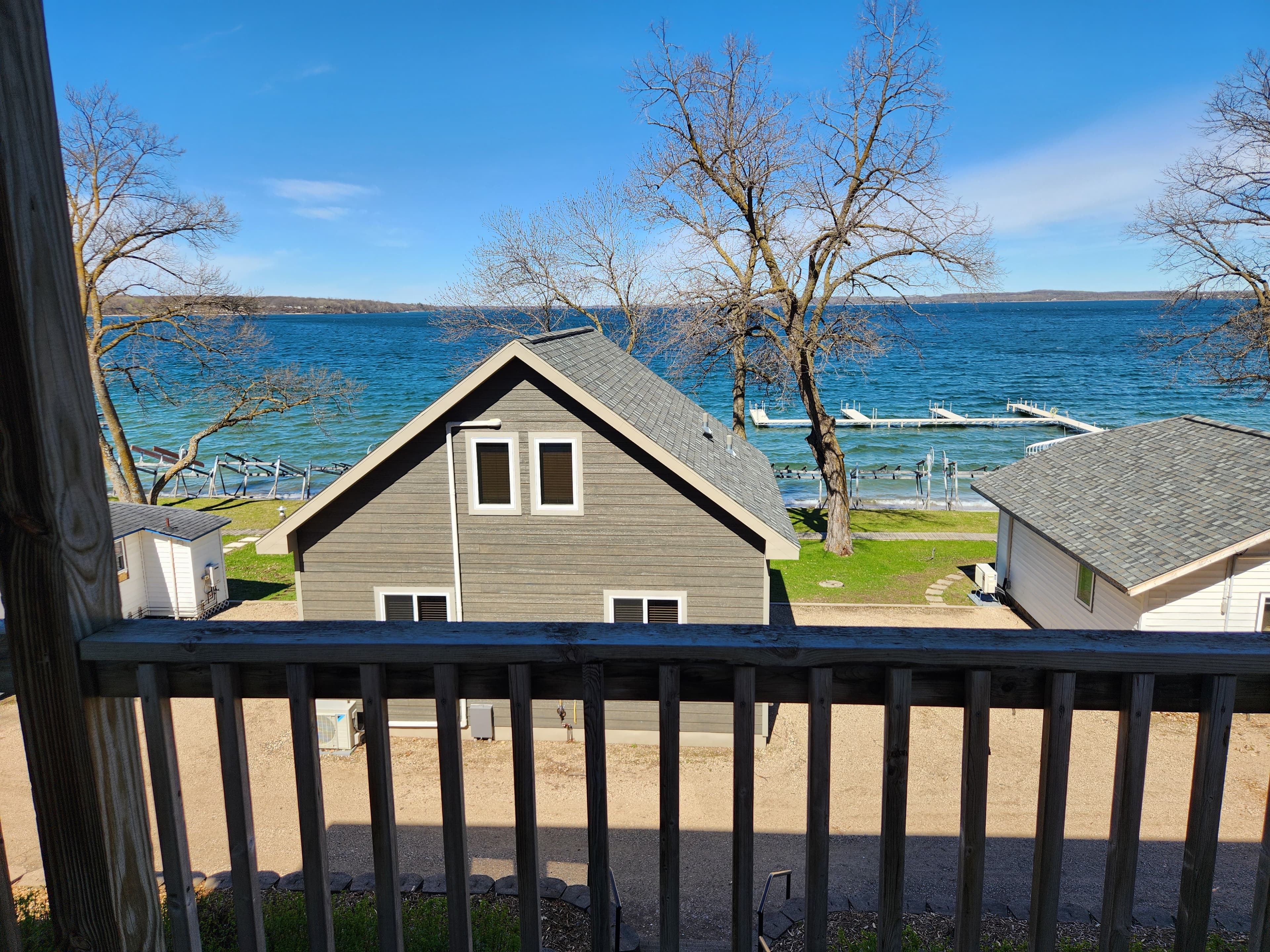 A view of a house by a lake with docks and bare trees under a clear blue sky.