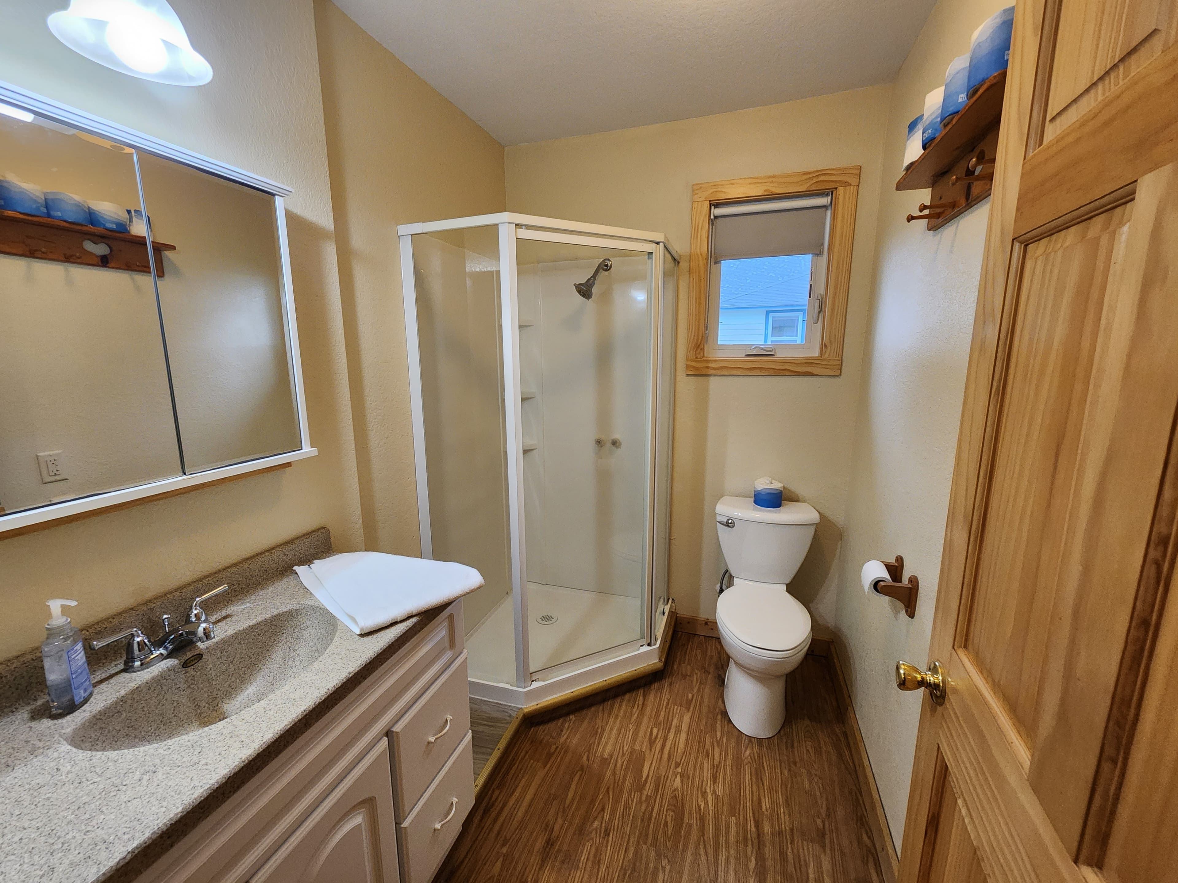 A well-lit bathroom featuring a shower, toilet, and sink with wooden accents and a mirror.