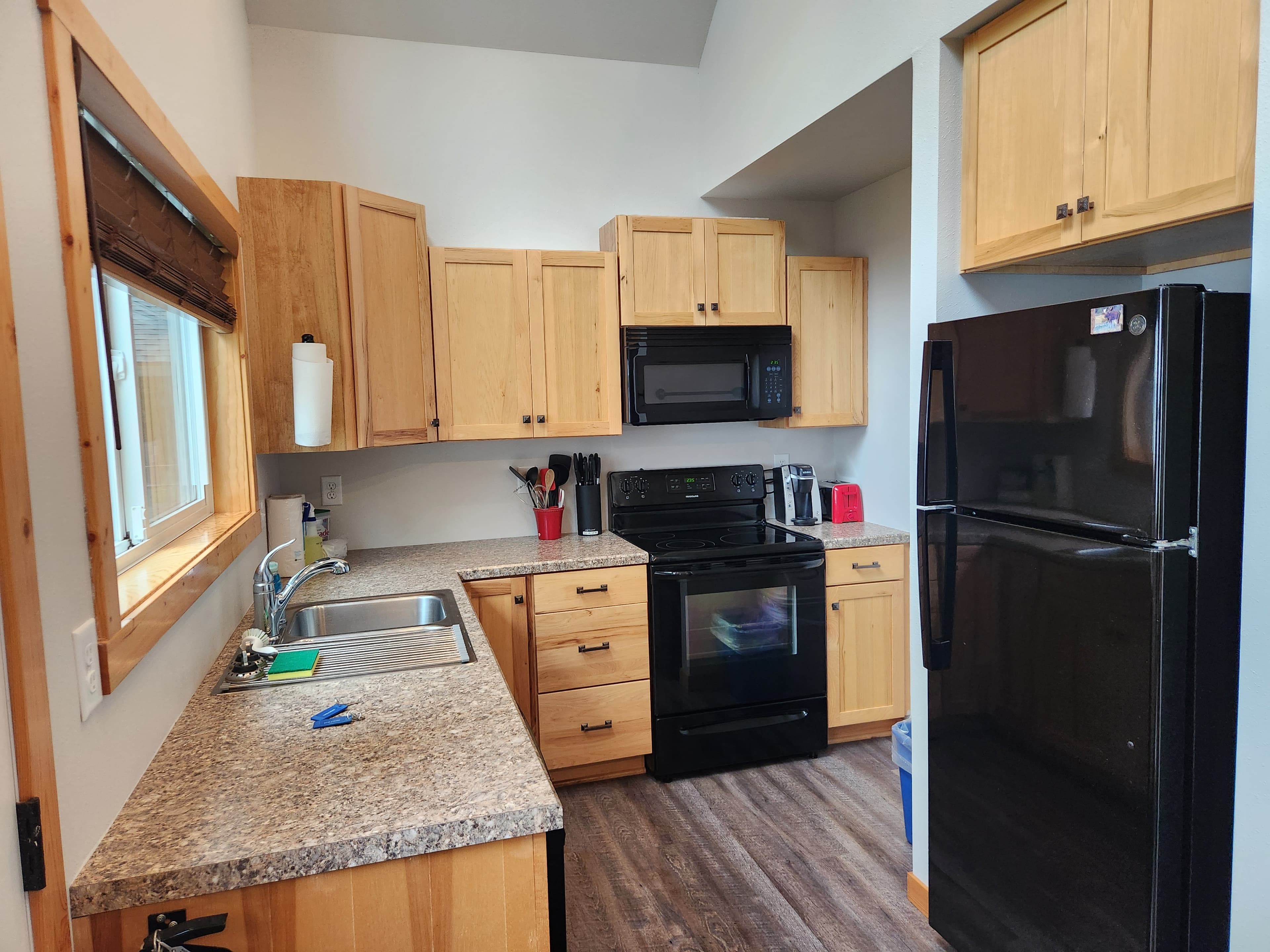 A modern kitchen featuring wooden cabinets, a black refrigerator, and stainless steel appliances.