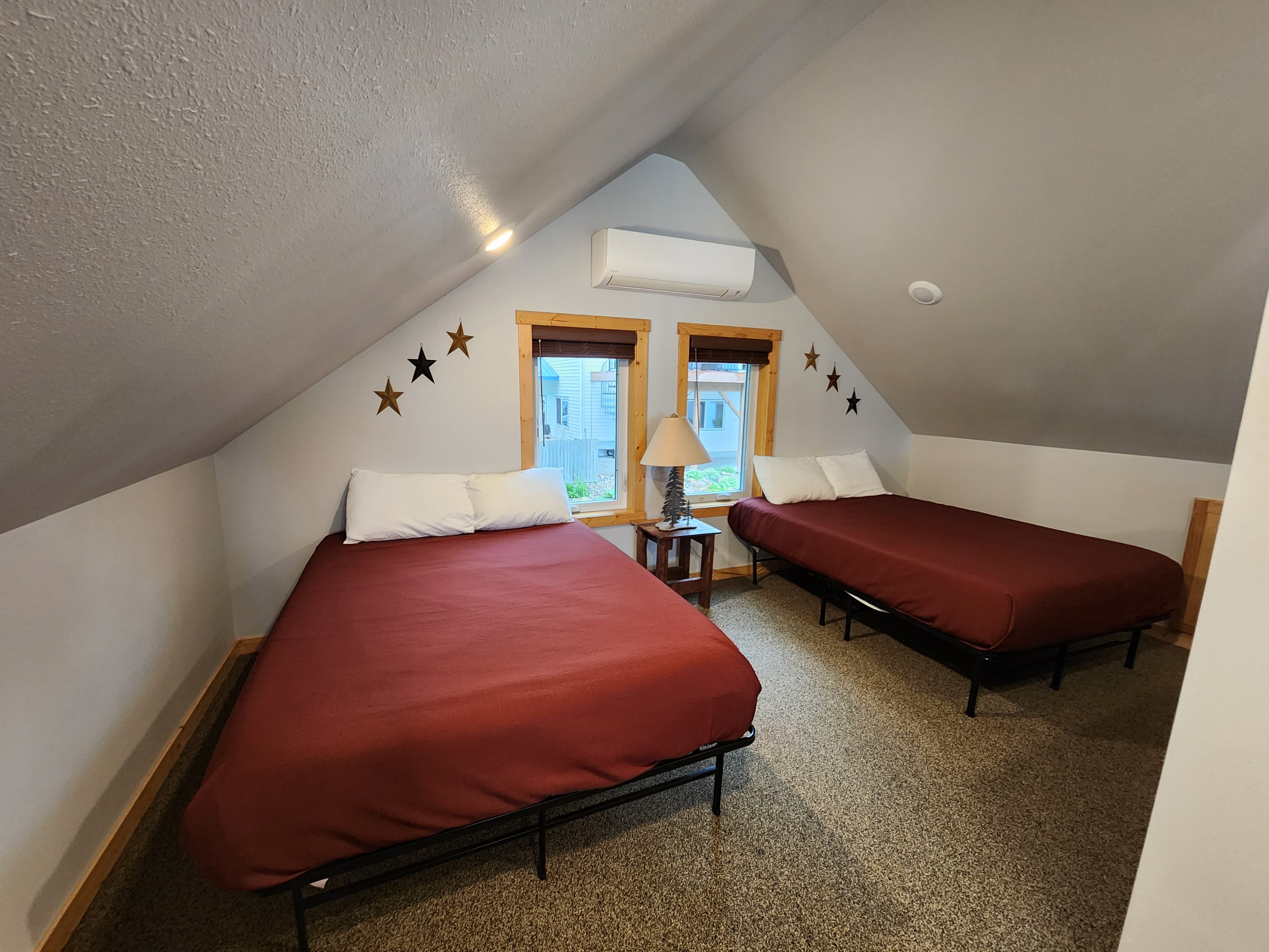 A cozy attic bedroom featuring two twin beds, a bedside table with a lamp, and star decorations on the wall.