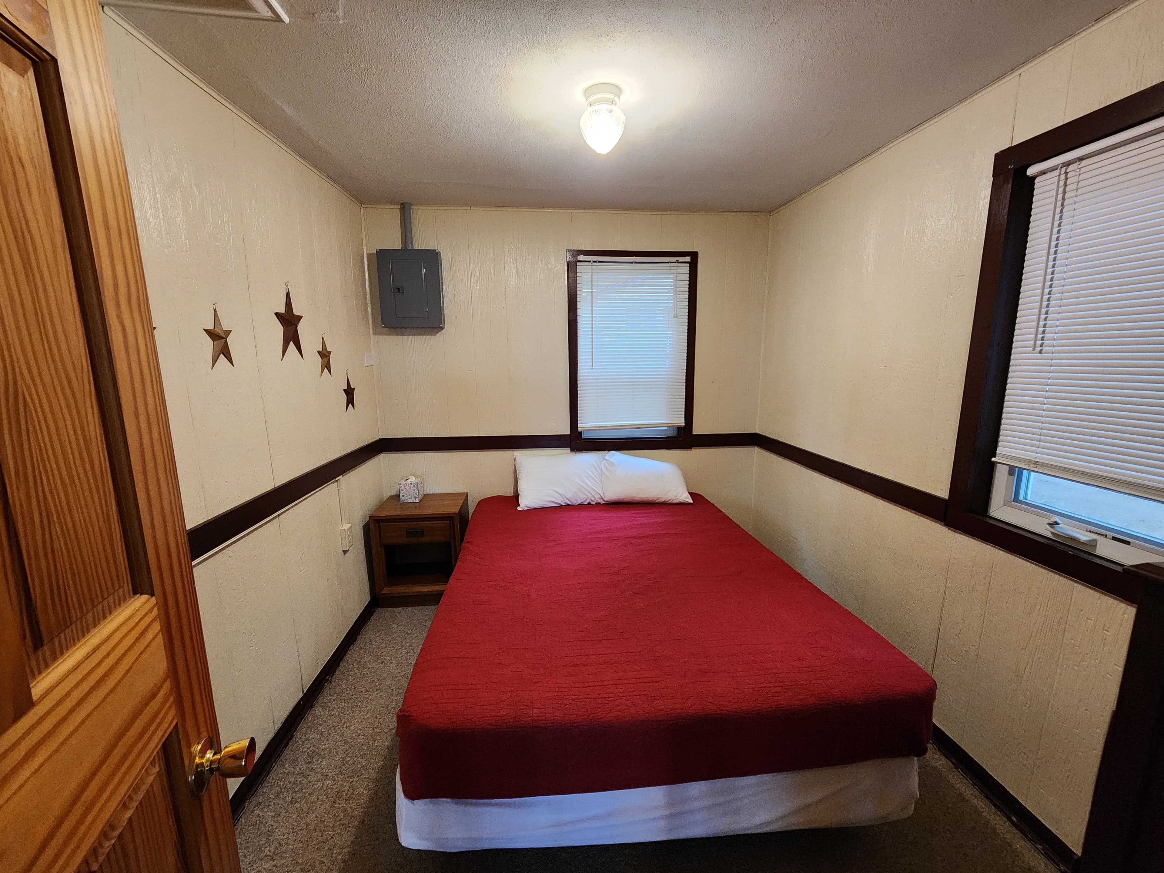 A small bedroom featuring a red bedspread, a bedside table, and star decorations on the walls.