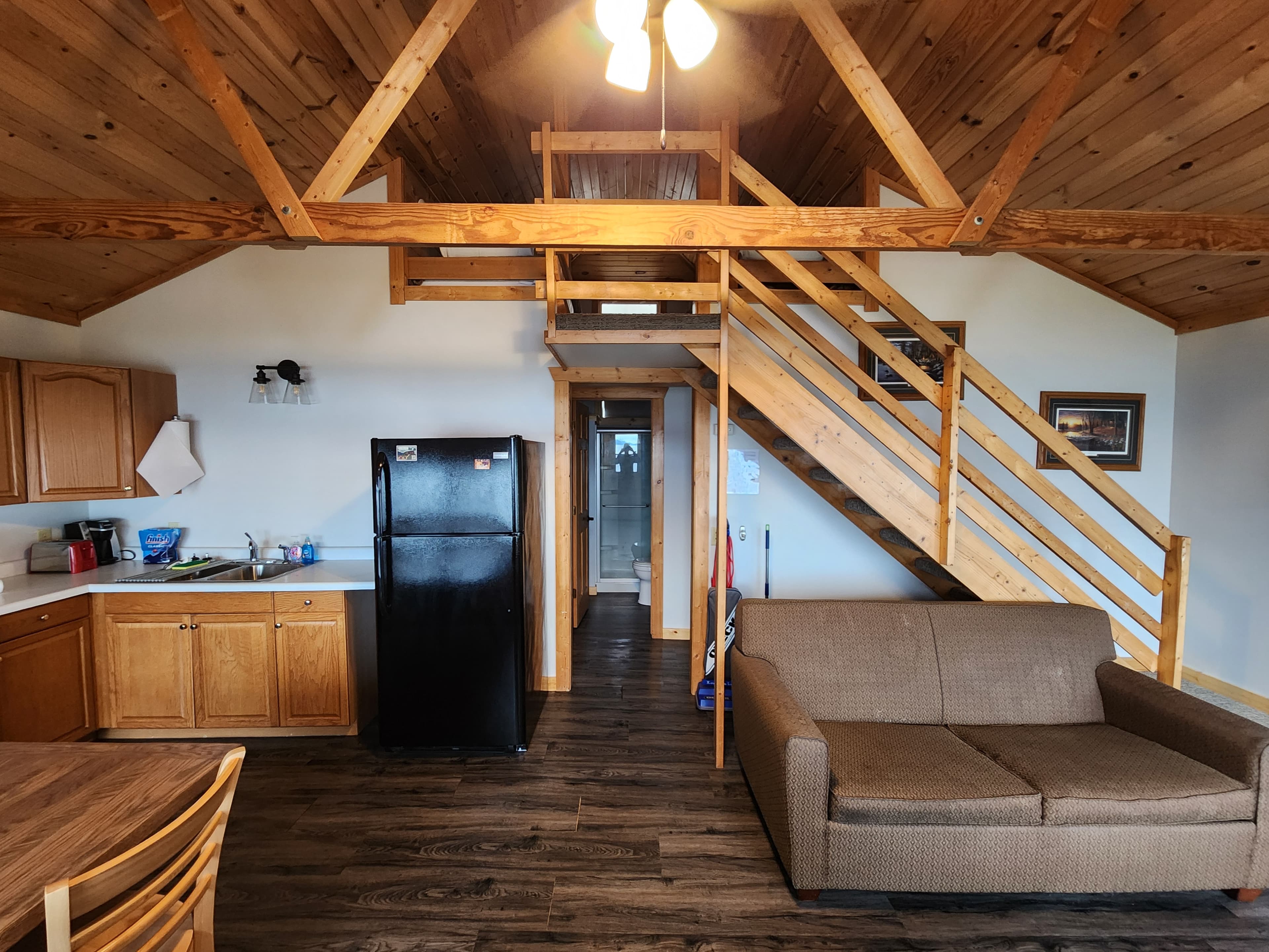 A cozy cabin interior featuring a kitchen, seating area, and a staircase leading to a loft.