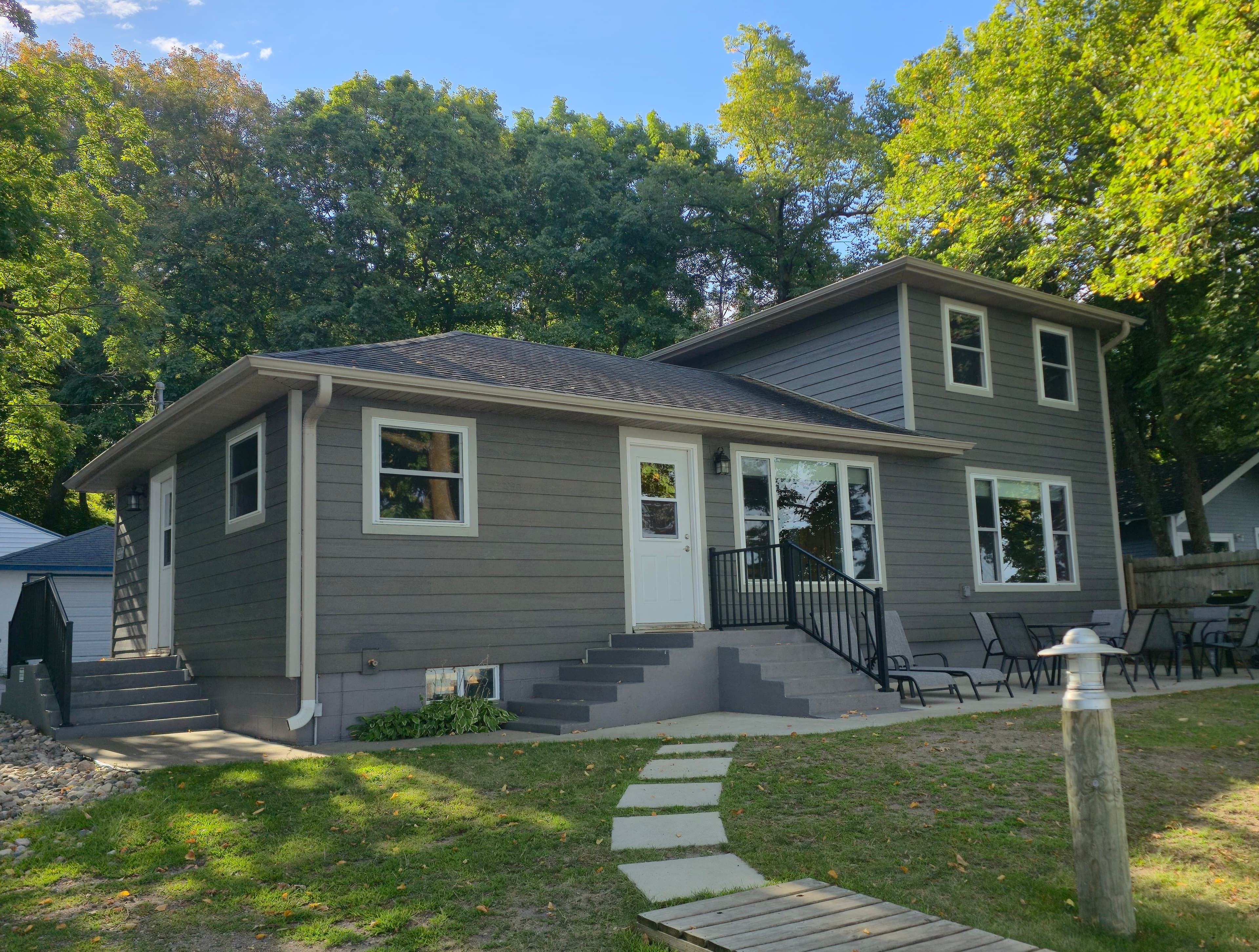 A modern gray two-story house with a welcoming front porch and surrounded by trees.