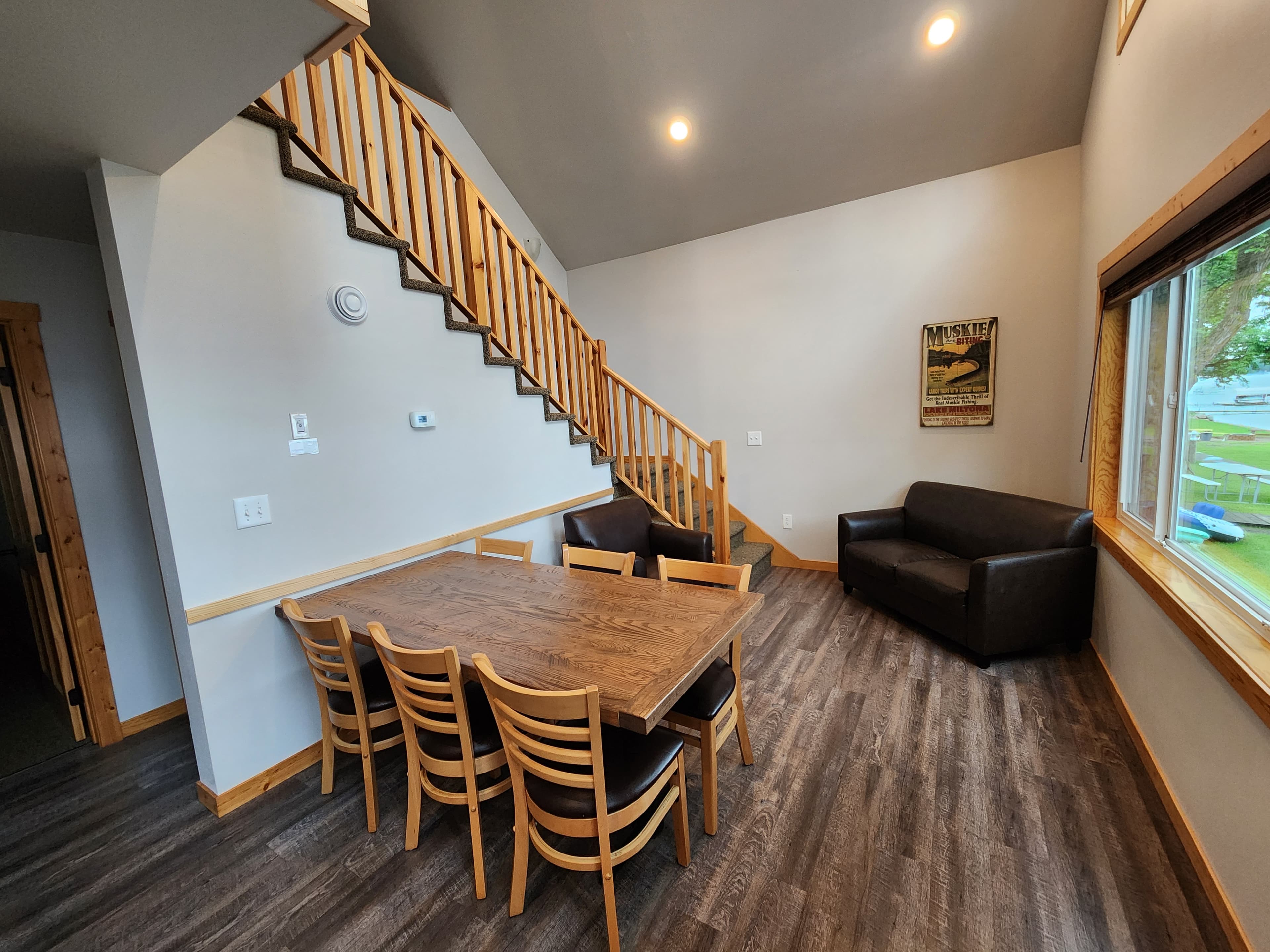 A cozy living space with a wooden dining table, chairs, a sofa, and a staircase leading to an upper level.